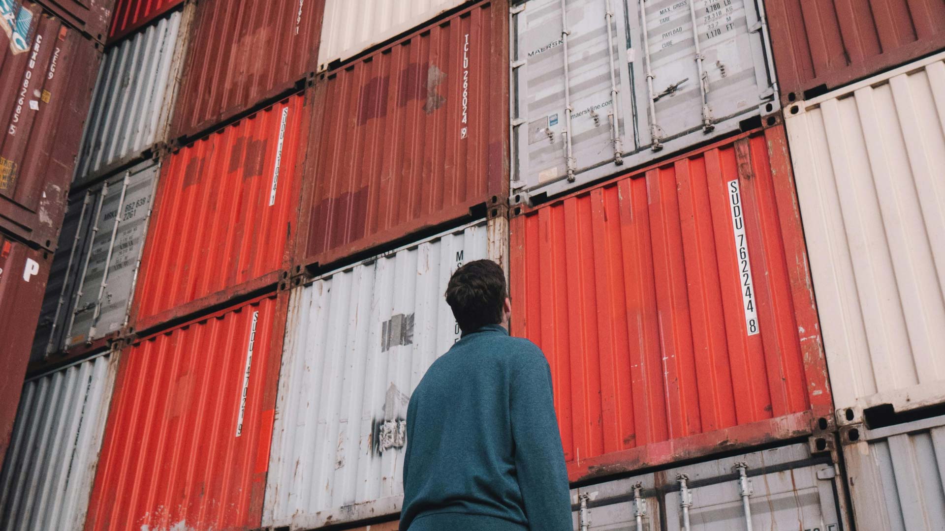 A man stands in front of containers and looks up.